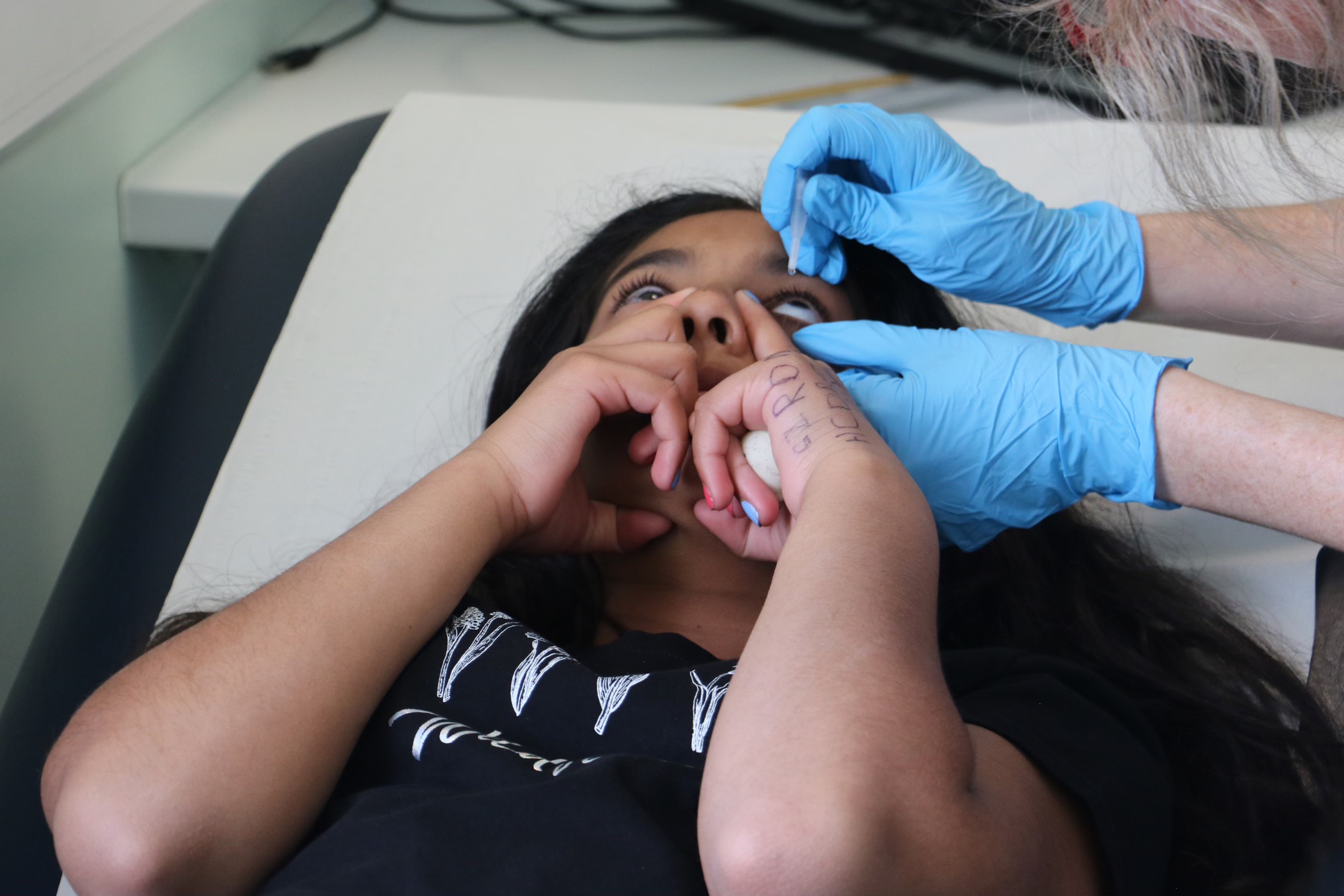 Consultant administering eye drops on a young person in a hospital consultation room
