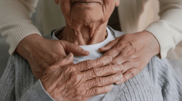 Older person sitting and holding the hands of someone standing behind them