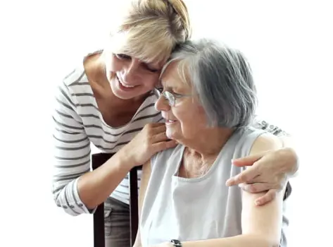 Two people, one sitting down with the other standing behind with their arms over their shoulders