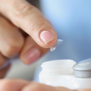 Image of a hand placing a contact lens in it's storage case.