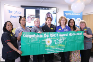 A group of seven Moorfields nurses holding the Daisy Award banner smiling at the camera