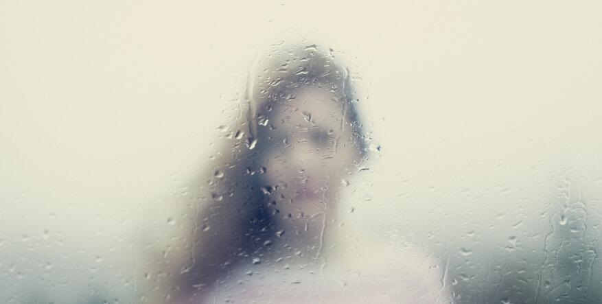 A photo of a young woman through a rainy window