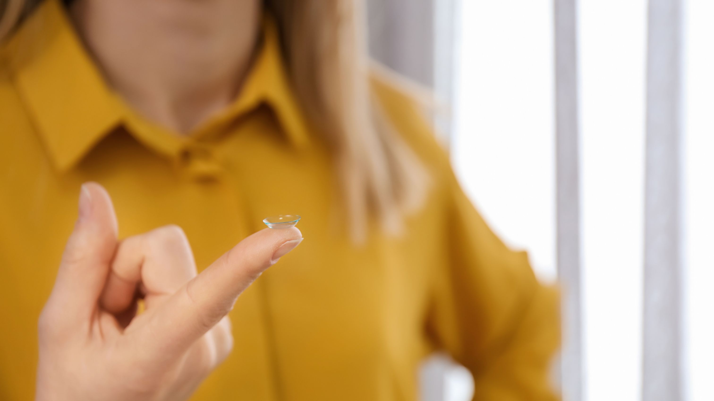 Contact lens on the finger of a person wearing a yellow shirt