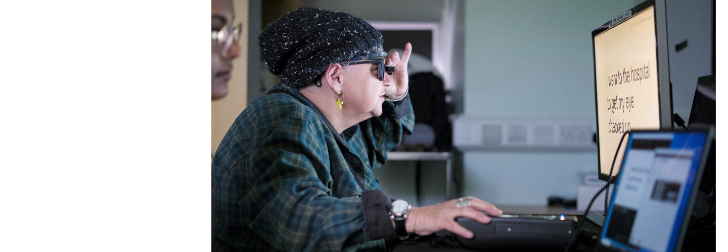 Patient in a darkened consultation looking at a bright white computer screen, wearing specialist glasses 