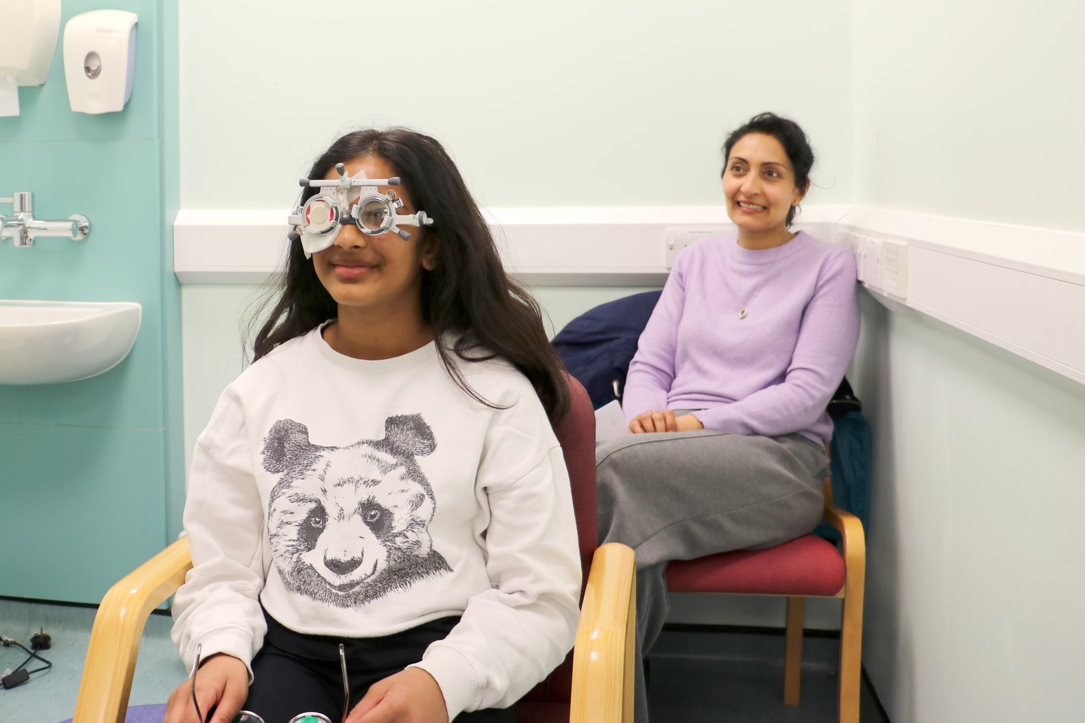 Young person in a consultation room with testing glasses, a grown up is sitting behind them