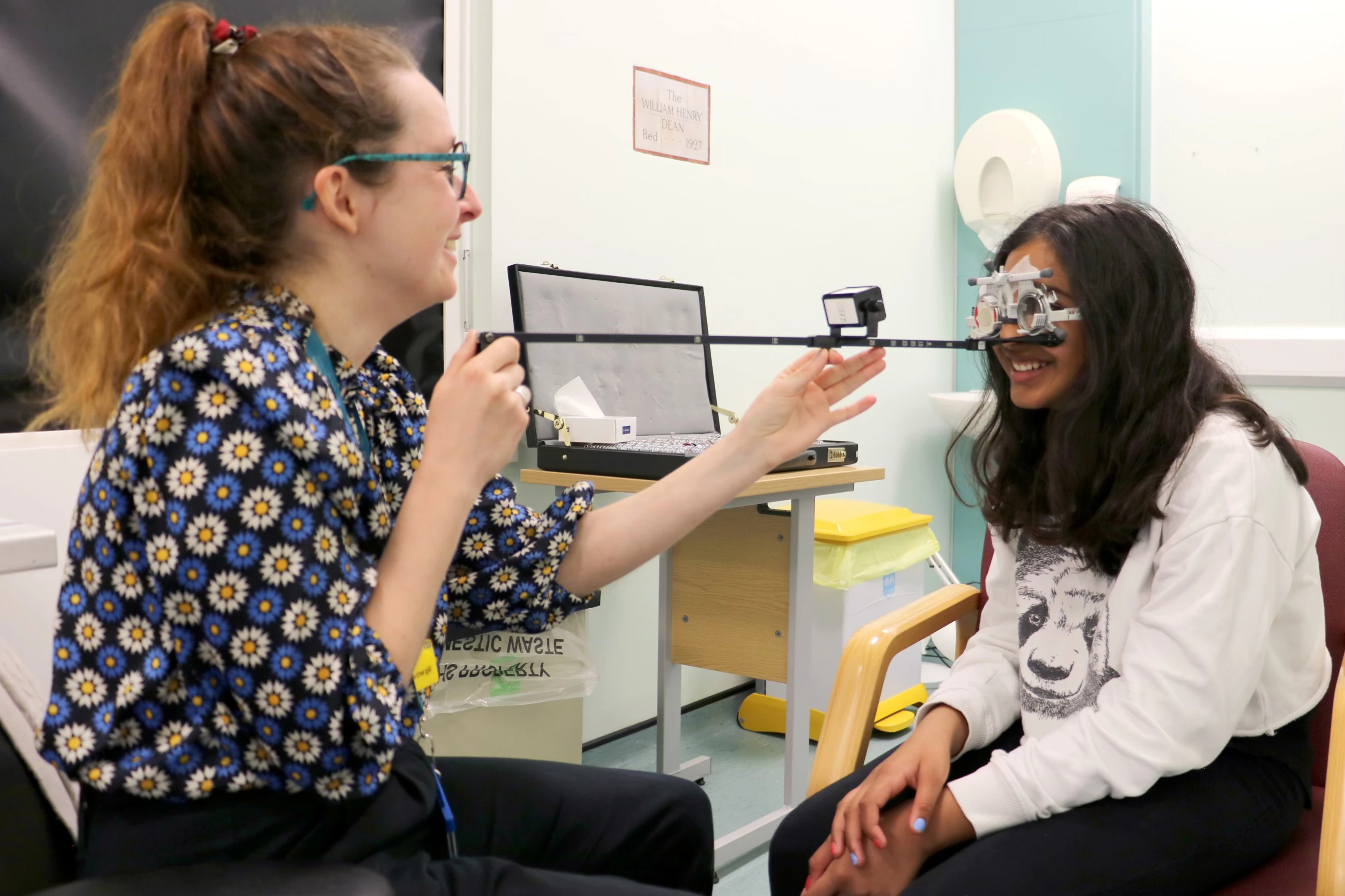 Two people in a consultant room with a child reading letters on a ruler